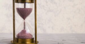 Eine traditionelle Sanduhr mit rosa Sand, die Zeit und Geduld auf einer strukturierten Oberfläche symbolisiert.