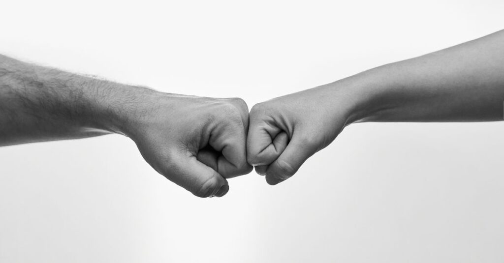 Ausdrucksstarkes Schwarzweißbild zweier aufeinander zugekniffener Fäuste, Symbol für Einheit und Freundschaft.