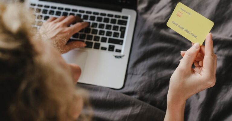 Person, die eine Kreditkarte für Online-Einkäufe auf einem Laptop verwendet, von oben aufgenommen.