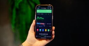 Nahaufnahme einer Hand, die ein Smartphone hält, das eine Aktienhandels-App mit Echtzeitdaten anzeigt.