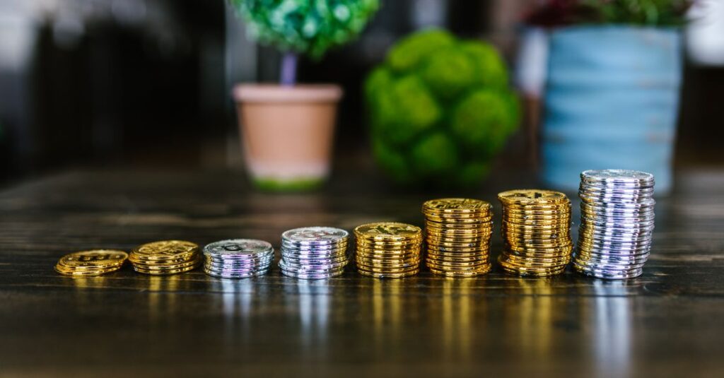 Nahaufnahme von gestapelten Gold- und Silber-Bitcoins auf einem Holztisch mit Pflanzen im Hintergrund.